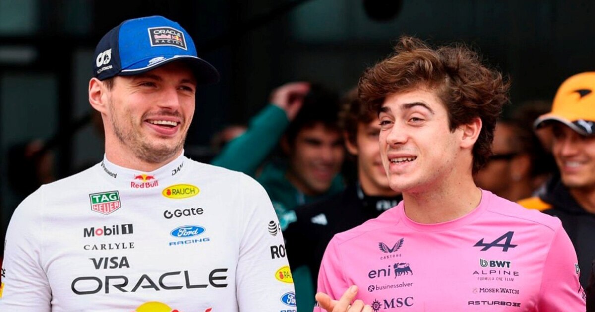Dos pilotos de automovilismo conversan sonrientes vistiendo sus respectivos uniformes de equipo en un evento deportivo.