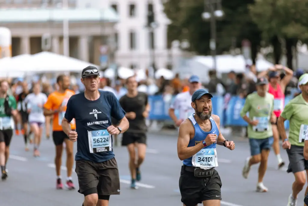 Corredores masculinos en el Maratón de Berlín con dorsales numerados y edificios históricos al fondo de la imagen.