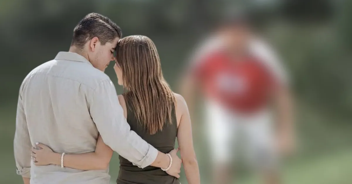 Pareja abrazada de espaldas frente a una imagen difuminada de un video viral en el fondo.