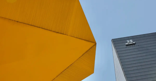 Edificio con el logotipo del SAT junto a una estructura arquitectónica amarilla bajo un cielo despejado.